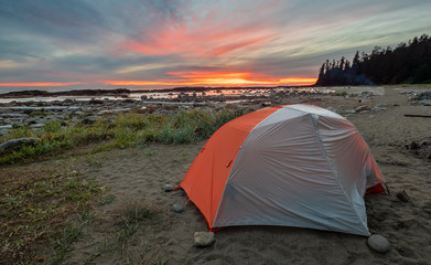 Backpacking tent on a beach with amazing dramatic sunrise in the distance.