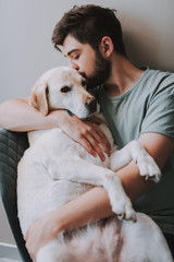 Delighted young man embracing his dog while kissing it and expressing love