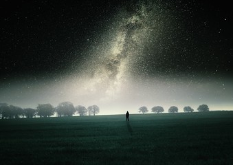 Dreamy surreal landscape with starry night sky and man silhouette