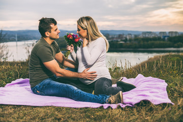 Husband giving flowers to his pregnant wife while enjoy spending time together outdoor.