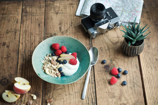 Breakfast bowl with granola, yogurt, nuts, apple, raspberry, blueberry on wood