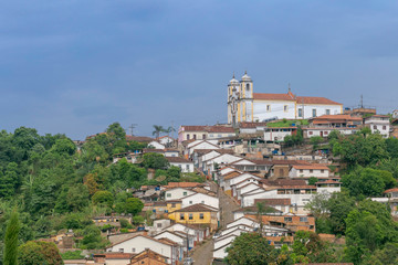 Casarão colonial no centro histórico de Ouro Preto, em primeiro plano, e Igreja de Santa Ifigênia ao fundo com casario em ladeira abaixo, em Ouro Preto, Brasil