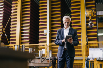 Successful entrepreneur standing in his company, using digital tablet
