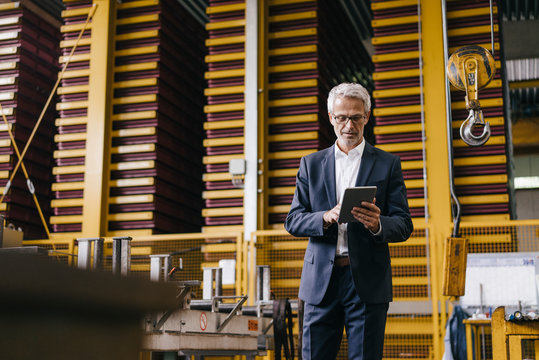Successful entrepreneur standing in his company, using digital tablet