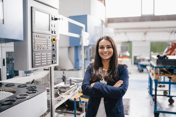 Confident woman working in high tech enterprise, standing in factory workshop with arms crossed