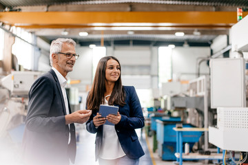 Businessman an woman in high tech enterprise, having a meeting in factory workshop