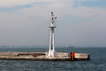 Lighthouse on the sea under the sky. A white sea lighthouse in the middle of the harbor points the path of ships at night and foggy time with light.