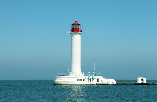 Lighthouse on the sea under the sky. A white sea lighthouse in the middle of the harbor points the path of ships at night and foggy time with light.