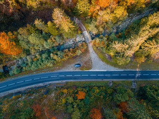 Aerial view of a road in Gruyère, Switzerland. Car parked in the middle of a place with tall trees during an autumn in Europe. Drone view.