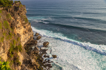 Ocean with rocks and cliff in Uluwatu, Bali at sunset light