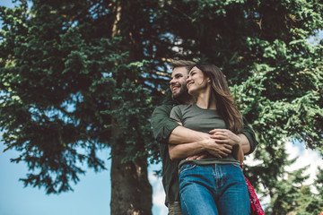Take a break and relax together. Low angle portrait of young man embracing his girlfriend while standing on green tree background