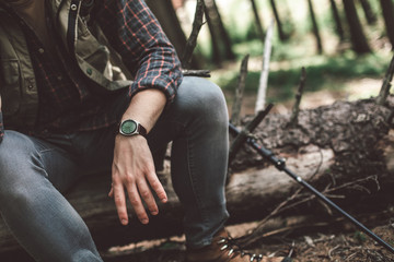Have a rest in journey. Close up low angle portrait of young male traveler sitting on the balk in green forest. Copy space on right