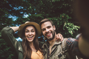 Concept of enjoying journey and adventure in couple. Close up portrait of excited smiling man and woman making selfie in sunny green forest