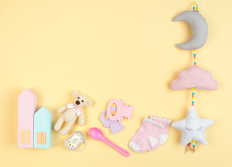 Baby girl accessories and toys on yellow background with copy space
