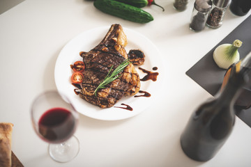 Top view of white kitchen table with delicious seasoned meat, glass of wine, bread, cucumber and onion