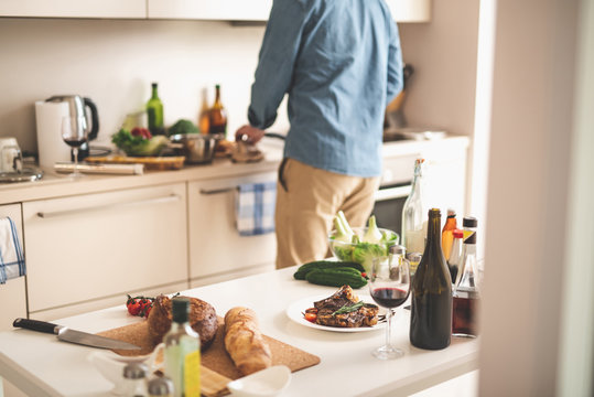 White Kitchen Desk With Delicious Seasoned Meat, Glass Of Alcohol Drink And Bakery. Cropped Gentleman Cooking Dinner Near Stove