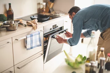 Foto op Plexiglas Portrait of gentleman in denim shirt closing door of oven while looking at frying pan with beef steak © Yakobchuk Olena