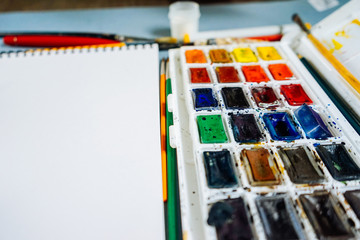 on a blue table is a drawing paper and colorful watercolor paints