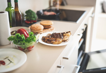 Kitchen table with roasted meat, vegetables, burger buns and paper towel