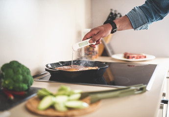 Close up of male hand checking readiness of meat on frying pan