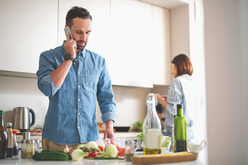 Important call. Waist up portrait of young gentleman in denim shirt having phone conversation. Young lady on blurred background