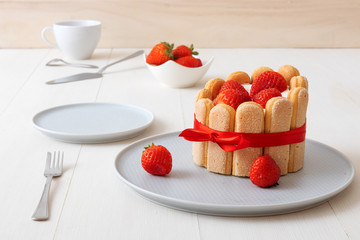 Charlotte, French dessert with strawberries, tied up with a scarlet ribbon, coffee cup, bowl with strawberries on white table.