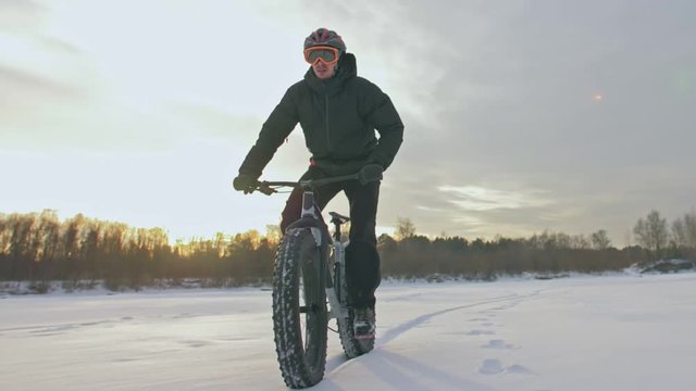 Professional extreme sportsman biker riding fat bike in outdoors. Cyclist ride in winter snow forest. Man does trial trick wheelie on mountain bicycle with big tire in helmet and glasses.