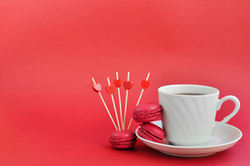 Bright concept for Valentine's day. Cup of tea and raspberry macaroons on red background. Trending Panton color