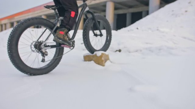 Professional extreme sportsman biker riding fat bike in outdoors. Cyclist ride in winter snow forest. Man does trial trick pedal kick jump on mountain bicycle with big tire in helmet and glasses.
