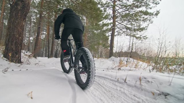 Professional extreme sportsman biker riding fat bike in outdoors. Close-up view of rear wheel. Cyclist ride in winter forest. Man on mountain bicycle with big tire. Snow fly into the lens camera.