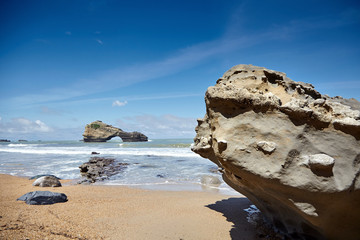 Stones on a sandy beach and a rocky island with a hole. Ocean waves. Atlantic coast in southwestern...