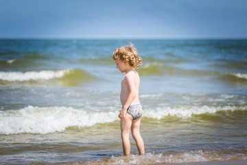 Fototapeta na wymiar Young caucasian boy playing on sea shore at sunny summer