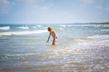 Young caucasian boy playing on sea shore at sunny summer
