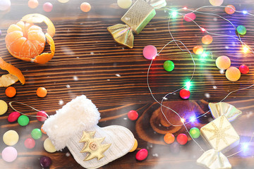 Christmas toys and garland on a wooden table. Tangerines, candy, confetti. Greeting card, top view, blur, place for text.