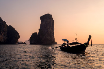 Sunset with silhouette of Traditional Longtail boat and High rock in the sea. Thailand