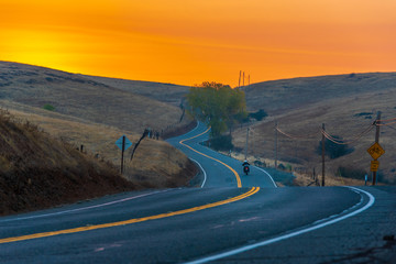 Motorcycle traveling down a winding country road at sunrise.