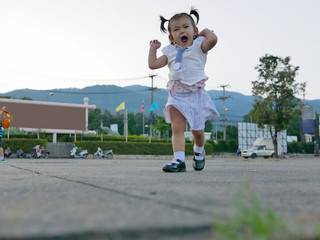 Obraz premium Little Asian baby girl, 19 months old, enjoys running on an outdoor concrete floor