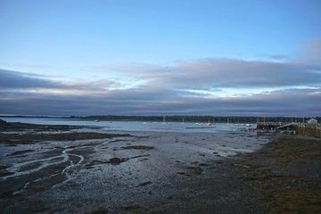 St. Andrews, New Brunswick, Canada: The harbor in the Bay of Fundy at low tide, in the early morning, with dramatic cloud formations overhead and small boats in the distance.