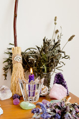 Purple beeswax candle, besom and dried herbs on altar with crystals