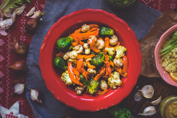 Baked roasted vegetables for Christmas lunch or dinner on red tablecloth. Vegan food with brussels sprouts, carrots, cauliflower, mushrooms. Social network trendy color style. In red bowl or plate