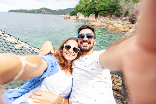 Young beautiful happy smiling funny couple man and woman best friends on a hammock on vacation makes selfie on a smartphone against the background of the sea