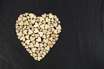 Obraz na płótnie Canvas Forming a large heart shape with small wooden heart shapes on black stone background.