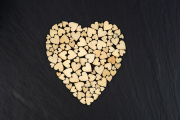 Forming a large heart shape with small wooden heart shapes on black stone background.