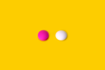 Two pills pink and white on a yellow background.