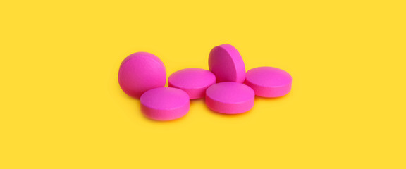 Several large pink tablets scattered on a yellow background. Side view.
