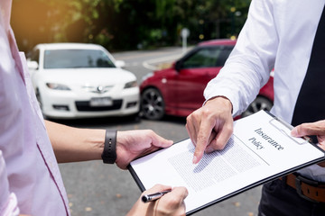 Insurance agent writing on clipboard while examining car after accident claim being assessed and...
