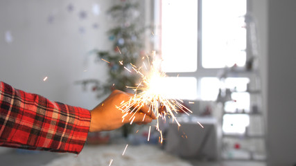 Girl's hand with burning sparkler in front of christmas tree