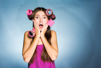 surprised young sad girl, on her head big pink hair curlers