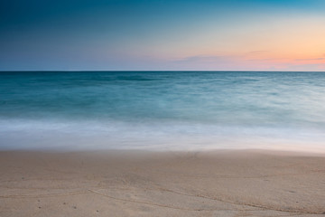 Fototapeta na wymiar soft wave at sea beach on blue sky and orange sun set, long exposure shot