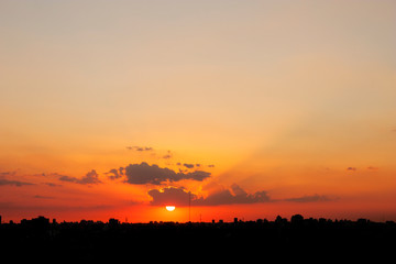 Fototapeta premium Sun hanging from cloud above backlit city skyline in big general shot and aerial view